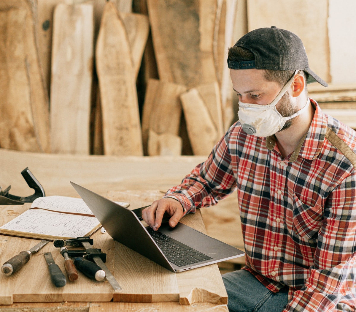 Man with mask over his face on his laptop, while tools lay on his side.