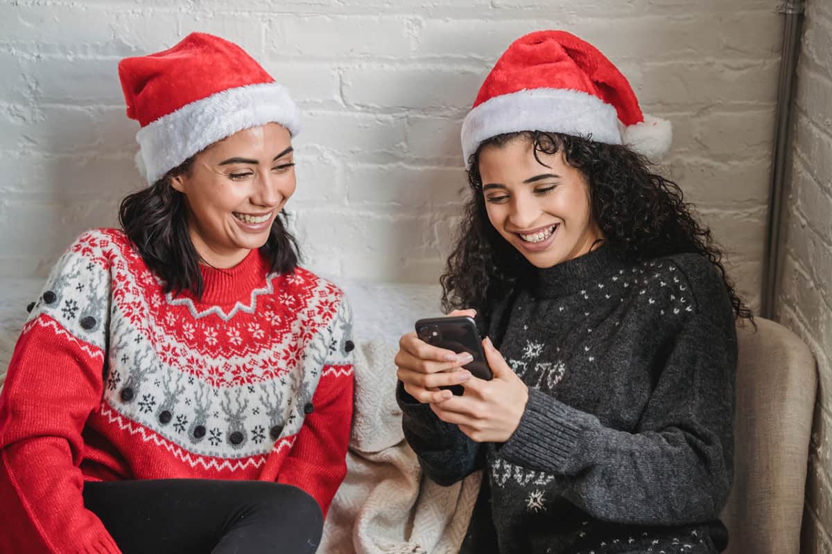 two people wearing santa hats looking at mobile phone
